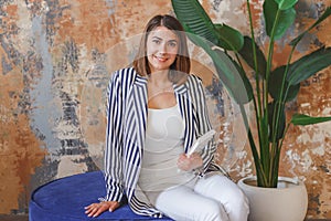 Woman in striped jacked posing in front of big plant. Indoor interior portrait