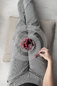 Woman with striped pants and a bowl of red, fresh and ripe cherries