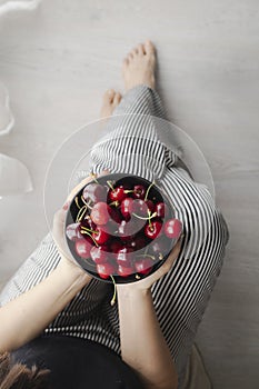 Woman with striped pants and a bowl of red, fresh and ripe cherries