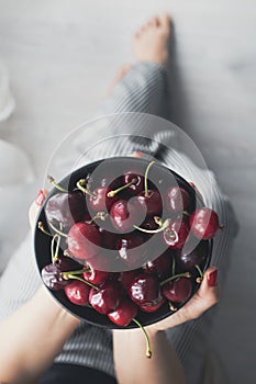 Woman with striped pants and a bowl of red, fresh and ripe cherries