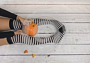 Woman in striped stockings preparing pumpkin for Halloween