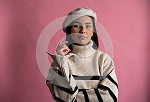 Woman in striped sweater and beret, smiling in front of pink background