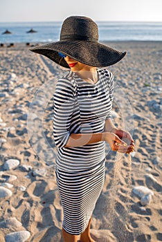 Woman in stripped dress with a hat on the beach