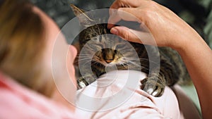 A woman strokes a cat that lies on her chest.