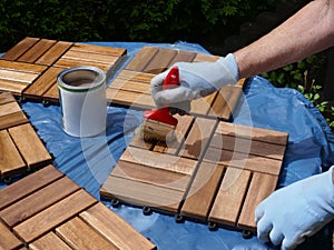 A woman strokes wood preservation glaze on square wood panels to make them weatherproof.