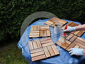 A woman strokes wood preservation glaze on square wood panels to make them weatherproof.