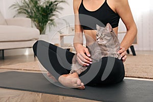 Woman stroking her cat while practicing yoga at home, closeup