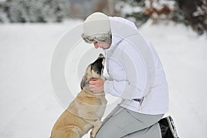 Woman is stroking light color puppy on white snow