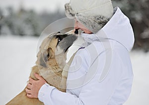 Woman is stroking light color puppy on white snow