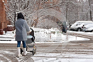 A woman with a stroller and a child goes into heavy snow. Walk with the baby in the pram. Badly cleaned streets of snow, the