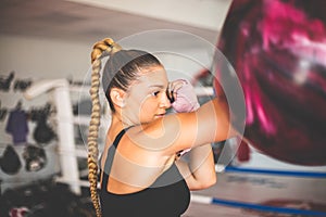 Woman, strong young lady with boxing gloves, punching a punching bag in gym alone