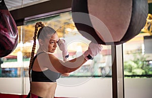 Woman, strong young lady, punching a  bag in gym alone. Focus is on woman.  alone. Focus is on woman