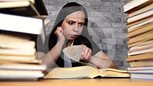 Woman student boring reading book at library with a lot of books in university. Student disheartened reading book for