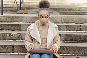 woman student e-learning distance training course study working on stairs in the city. African Ethnicity young woman