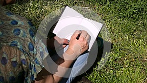 Woman and student sitting on grass, takes notes in notebook, learning and writes thoughts, writes book.