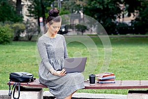 Woman student uses laptop on the bench at the park.