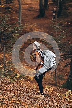 Woman in a stylish hat and travel bag on her shoulders, looking around at the charming autumn forest