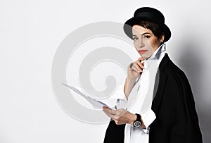 Woman in stylish old fashion boater hat and black jacket holding sheets of paper looks at us gravely photo