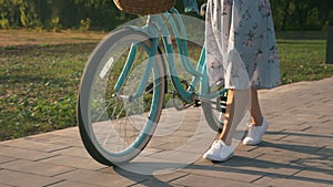 Woman in stylish outfit is walking with vintage retro bike in park in sunshine. Charming girl with bicycle in park at sunset. Bike