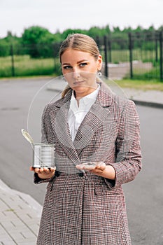 A woman in a stylish suit holds can of small dignity coins. The concept of quits, poverty and begging business ladies