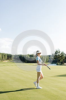 Woman in stylish summer golf outfit walking on beautiful green course for golf game