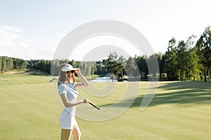 Woman in stylish summer golf outfit walking on beautiful green course for golf game