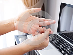 Woman suffering with aches and pains of hand and fingers from working with notebook computer on white table