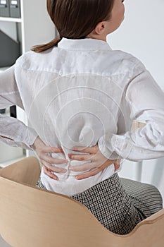 Woman suffering from back pain while sitting in office, closeup. Symptom of scoliosis