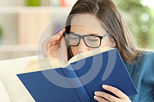 Woman suffering eyestrain reading a book with eyeglasses photo