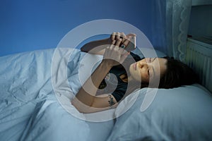 Woman suffering from internet addiction disorder, insomnia. Female using smartphone in bed at night