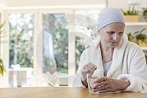 Woman suffering from ovarian cancer wearing bathrobe and headscarf taking pills at home. photo