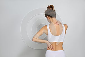 Woman suffering from pain in back on light grey background. Space for text