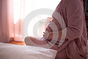 Woman suffering from pains at home, sitting at bed, touching her tummy and back, expecting lady having childbirth labo