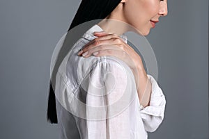 Woman suffering from shoulder pain on grey background, closeup