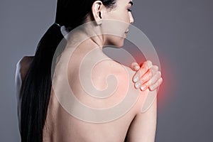 Woman suffering from shoulder pain on grey background, closeup