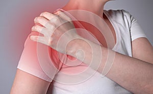 Woman suffering from shoulder pain. Hand holding shoulder with red spot closeup. Health problems, medicine concept
