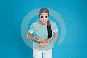 Woman suffering from stomach ache on light blue background. Food poisoning