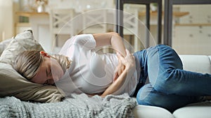 Woman suffering from stomachache lying down on sofa