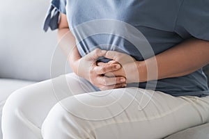 Woman suffering from stomachache sitting on the sofa at home. abdominal pain, Gastritis, Period, menstruation