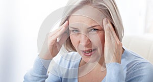 Woman suffering from stress or a headache grimacing in pain as she holds the back of her neck with her other hand to her