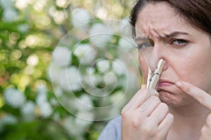 A woman suffers from a clothespin on her nose while walking in a flowery park. Allergy.