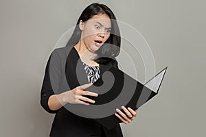 Woman in suit with angry shocked expression while holding and looking at folder