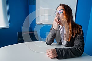 A woman in a suit and glasses makes yawns in the conference room. A female office manager with chronic fatigue sits at a
