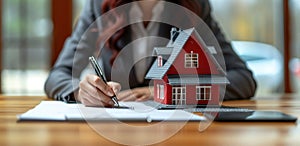 Woman in suit signing paperwork on home model making a real estate deal confidently, home loan paperwork image