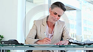 Woman in suit writing while sitting at her desk