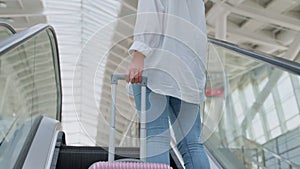 woman with suitcase on moving staircase, view from back, slow motion shot, female passenger