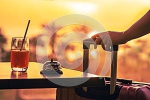 Woman with suitcase ringing hotel service bell with welcome drink and sea and palm tree view on sunset. Travel concept. 24-hour