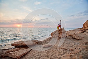 Woman with suitcase on rock watching nature sunset. Summer vacation, relaxation time and tourism concept. Copy space