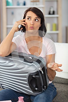 woman with suitcase on telephone making questioning expression