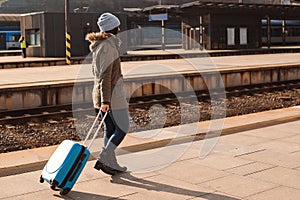 Woman with suitcase waiting for train on railway station. Winter travel, vacation and lifestyle